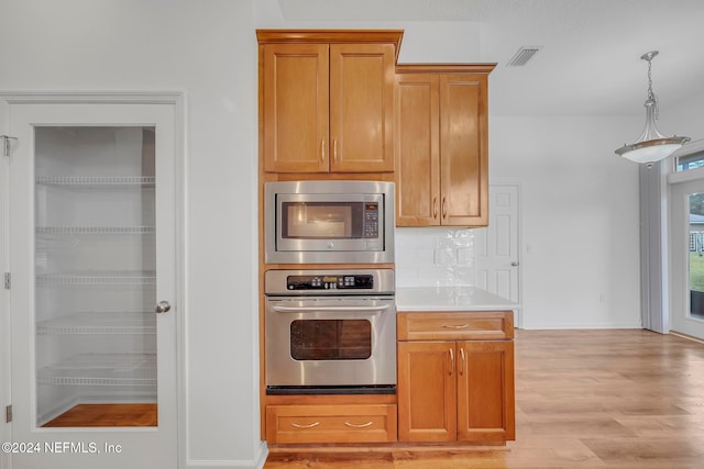 kitchen with decorative backsplash, light hardwood / wood-style floors, decorative light fixtures, and stainless steel microwave