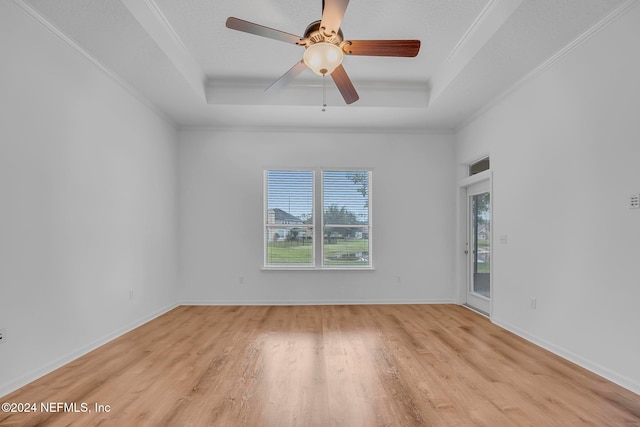 empty room with ornamental molding, light hardwood / wood-style floors, ceiling fan, and a tray ceiling