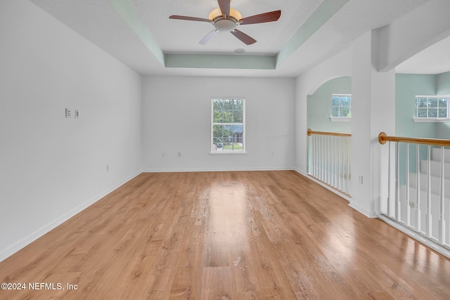 unfurnished room with light hardwood / wood-style floors, ceiling fan, a textured ceiling, and a tray ceiling