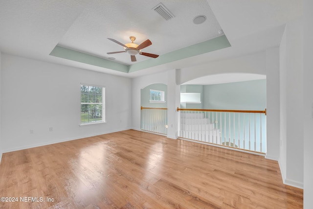 unfurnished room with light wood-type flooring, ceiling fan, and a raised ceiling