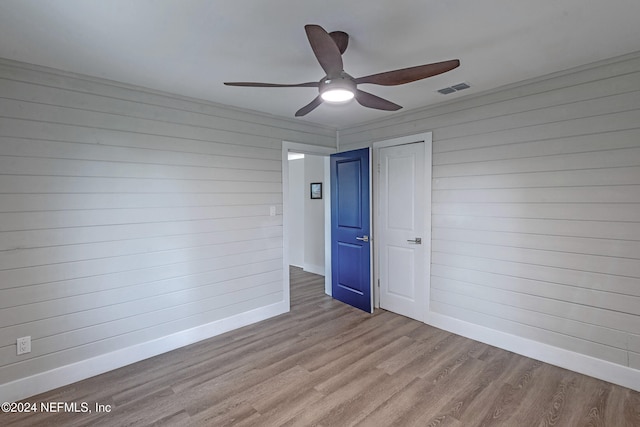 unfurnished room with ceiling fan, wooden walls, and light hardwood / wood-style flooring