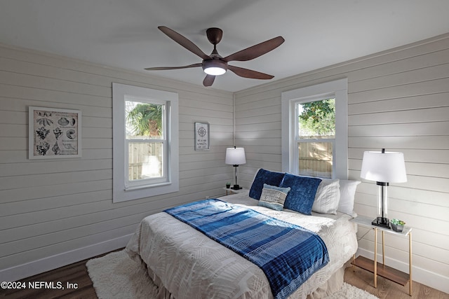 bedroom with wood walls, wood-type flooring, and ceiling fan