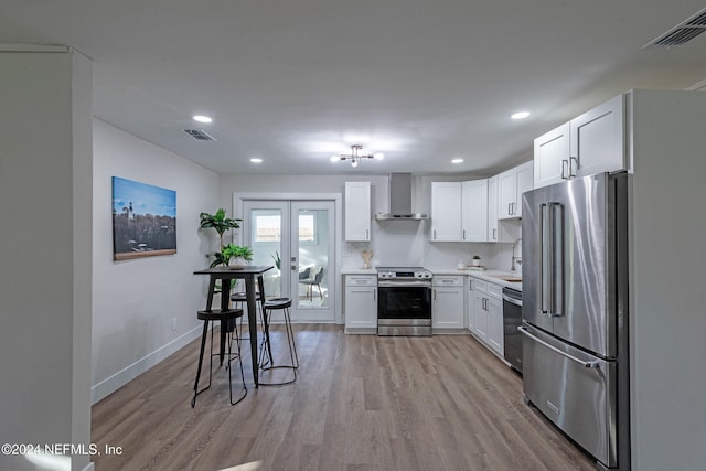 kitchen with stainless steel appliances, light hardwood / wood-style floors, wall chimney exhaust hood, white cabinets, and french doors