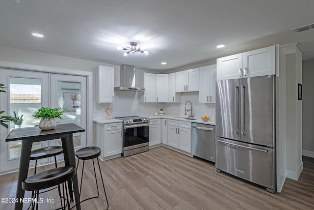 kitchen featuring stainless steel appliances, wall chimney range hood, sink, light hardwood / wood-style floors, and white cabinets