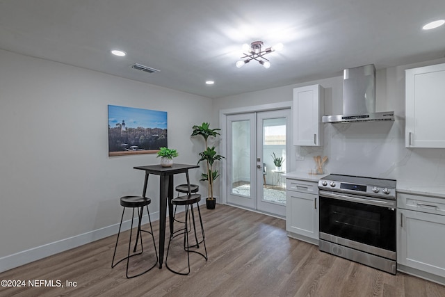 kitchen featuring french doors, stainless steel range, light hardwood / wood-style floors, white cabinets, and wall chimney exhaust hood