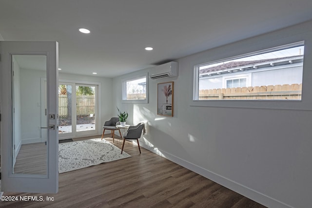 sitting room with a wall mounted AC, french doors, plenty of natural light, and dark wood-type flooring