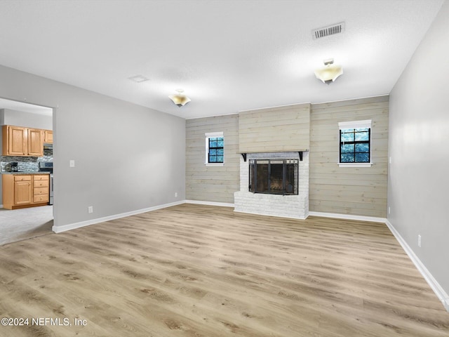 unfurnished living room featuring a textured ceiling, a fireplace, light hardwood / wood-style floors, and wooden walls