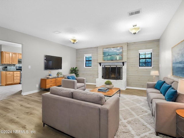 living room with a fireplace, light hardwood / wood-style floors, and wooden walls