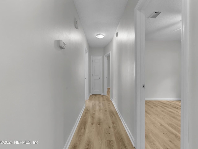 hall featuring light hardwood / wood-style floors and a textured ceiling