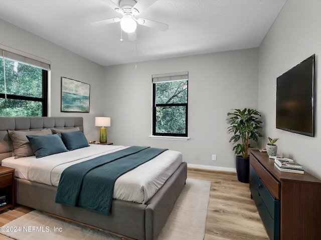 bedroom featuring a textured ceiling, light hardwood / wood-style floors, multiple windows, and ceiling fan