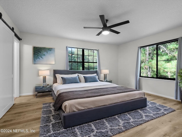 bedroom with a textured ceiling, a barn door, ceiling fan, and wood-type flooring