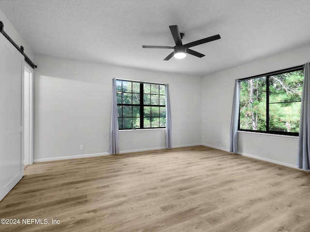 empty room with a textured ceiling, light wood-type flooring, a barn door, and ceiling fan