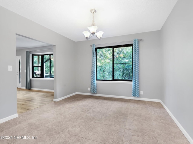 spare room featuring a wealth of natural light, light tile patterned floors, and an inviting chandelier