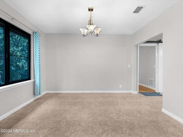 spare room featuring a barn door, light tile patterned flooring, a textured ceiling, and a notable chandelier