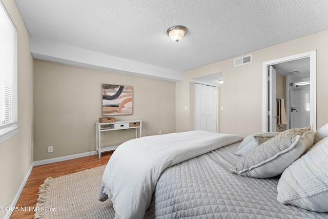 bedroom with wood-type flooring, connected bathroom, a textured ceiling, and a closet