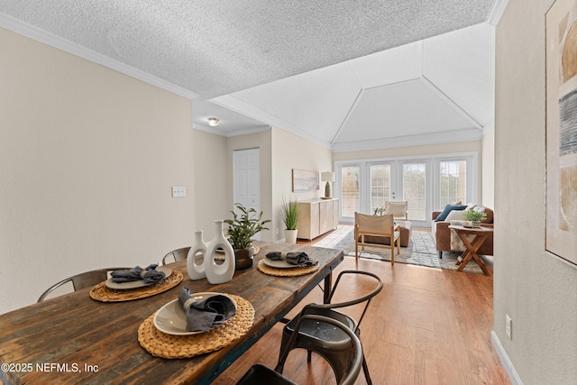 dining area with crown molding, lofted ceiling, a textured ceiling, and light hardwood / wood-style floors