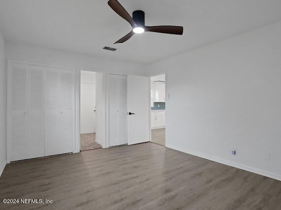 unfurnished bedroom with hardwood / wood-style flooring, ceiling fan, and two closets