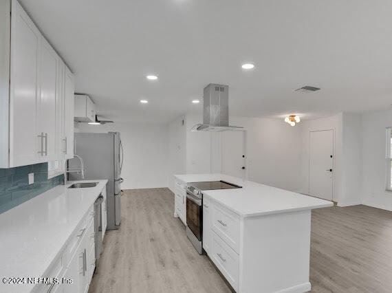 kitchen featuring stainless steel appliances, light hardwood / wood-style flooring, a kitchen island, white cabinets, and wall chimney range hood