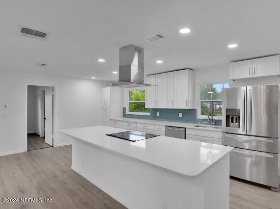 kitchen with white cabinets, wall chimney range hood, a kitchen island, and appliances with stainless steel finishes