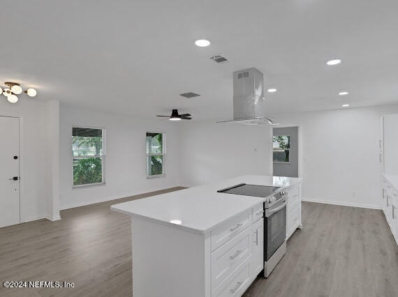 kitchen featuring stainless steel electric range, range hood, a kitchen island, light hardwood / wood-style floors, and white cabinets