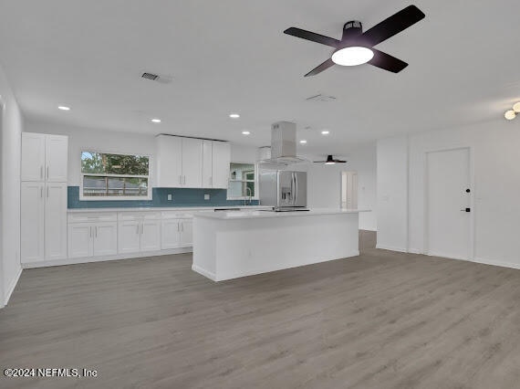 kitchen with white cabinets, light wood-type flooring, a kitchen island, and stainless steel fridge with ice dispenser