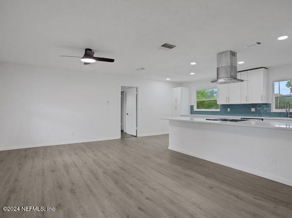 kitchen with hardwood / wood-style floors, a wealth of natural light, wall chimney exhaust hood, and white cabinetry