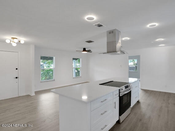 kitchen with light hardwood / wood-style floors, white cabinetry, ceiling fan, stainless steel electric stove, and wall chimney range hood