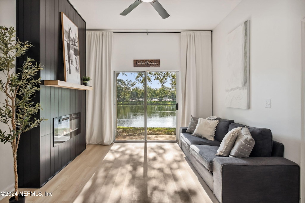 living room with light wood-type flooring, a water view, and ceiling fan