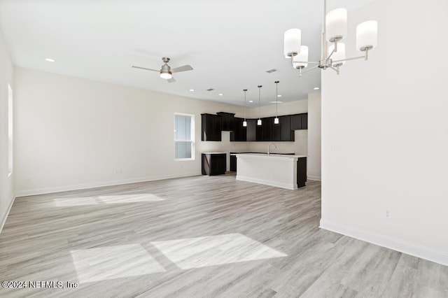 unfurnished living room featuring ceiling fan with notable chandelier and light wood-type flooring