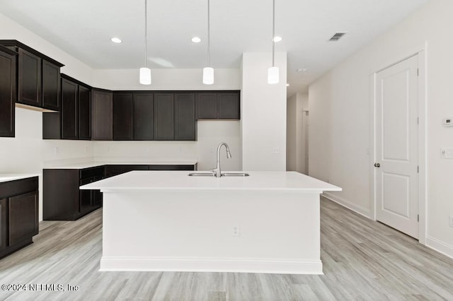 kitchen featuring a kitchen island with sink, light hardwood / wood-style flooring, sink, and decorative light fixtures