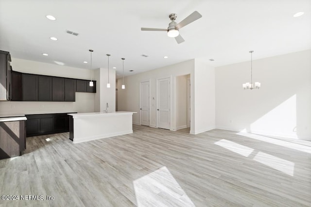 kitchen featuring sink, pendant lighting, ceiling fan with notable chandelier, an island with sink, and light wood-type flooring