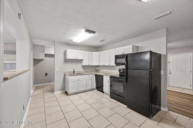 kitchen featuring black appliances, sink, light tile patterned floors, a textured ceiling, and white cabinetry