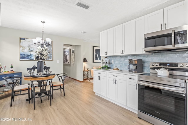 kitchen featuring appliances with stainless steel finishes, hanging light fixtures, light hardwood / wood-style flooring, a notable chandelier, and white cabinets