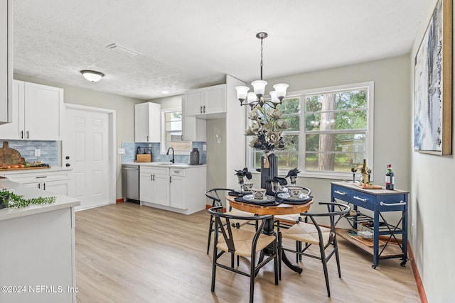 dining space featuring a textured ceiling, an inviting chandelier, sink, and light hardwood / wood-style flooring