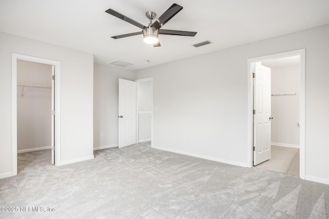 unfurnished bedroom with ceiling fan, a walk in closet, light colored carpet, and a closet