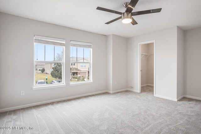 unfurnished bedroom with a walk in closet, light carpet, ceiling fan, and a closet