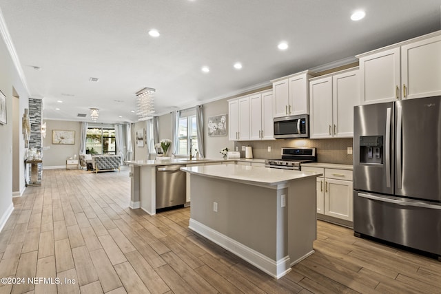 kitchen with white cabinets, light hardwood / wood-style floors, a kitchen island, and appliances with stainless steel finishes