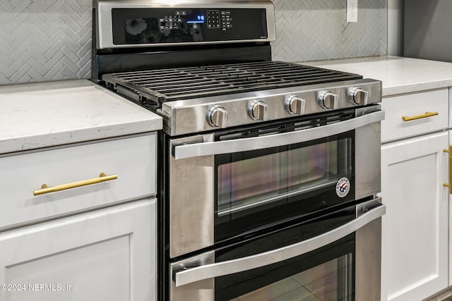 kitchen featuring white cabinets, light stone countertops, stainless steel gas stove, and tasteful backsplash