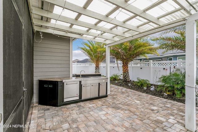 view of patio featuring an outdoor kitchen, a pergola, and sink