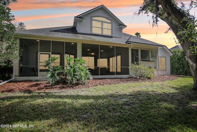 back house at dusk with a sunroom and a yard