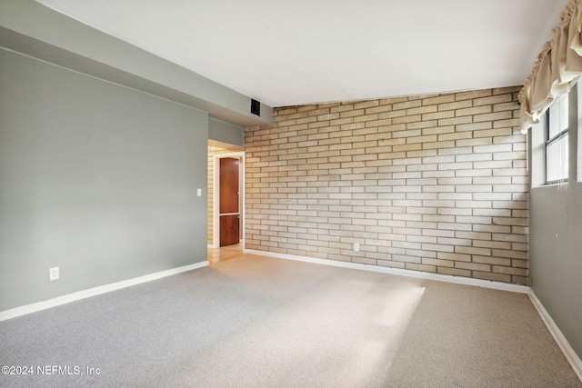 carpeted empty room featuring brick wall