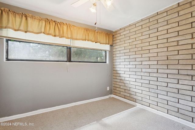 carpeted empty room with ceiling fan and brick wall