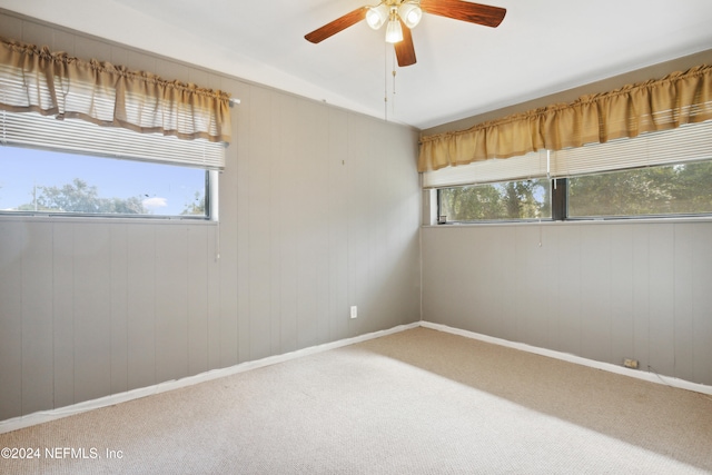 carpeted spare room with wood walls, ceiling fan, and plenty of natural light