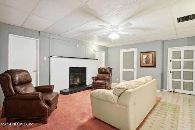 living room with a drop ceiling, light colored carpet, ceiling fan, and a brick fireplace