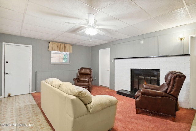 carpeted living room featuring a drop ceiling, ceiling fan, and a brick fireplace