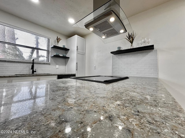 kitchen featuring sink, backsplash, dark stone counters, island range hood, and white cabinets