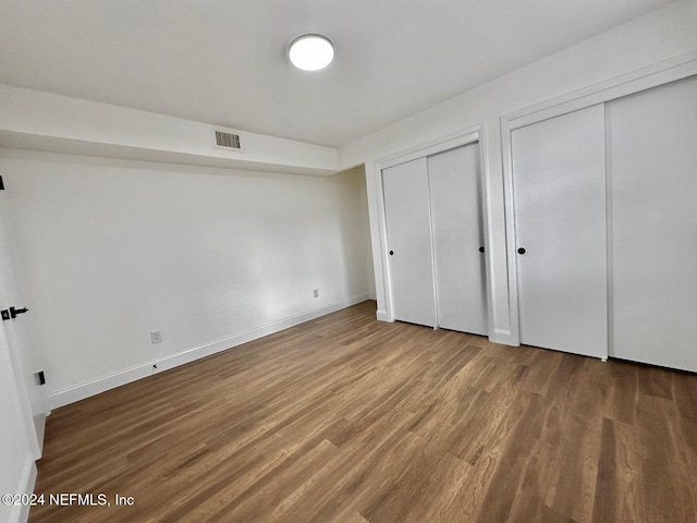 unfurnished bedroom featuring wood-type flooring and two closets