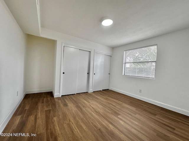 unfurnished bedroom with hardwood / wood-style floors and two closets