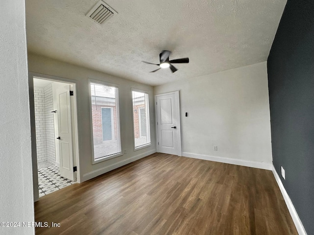 empty room featuring a textured ceiling, dark hardwood / wood-style flooring, ceiling fan, and brick wall