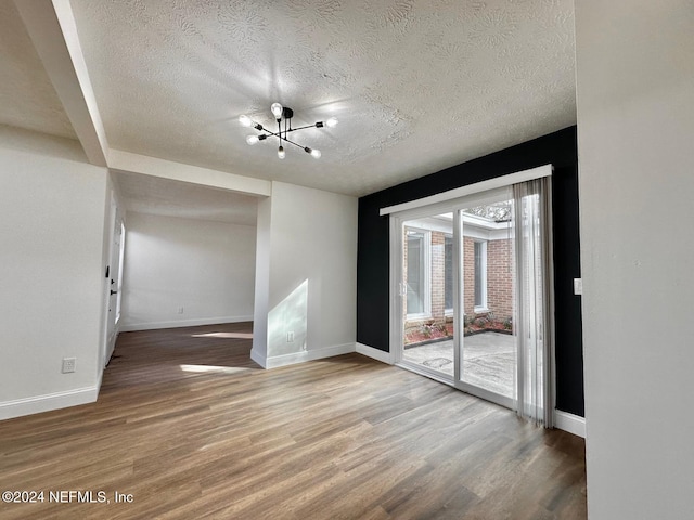 empty room featuring wood-type flooring, a textured ceiling, and a notable chandelier